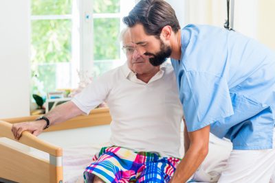 Elderly care nurse helping senior from wheel chair to bed